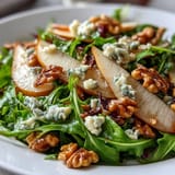 Fresh arugula and sliced ripe pears topped with crumbled blue cheese and crunchy toasted walnuts in a bowl.