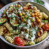 Colorful roasted vegetables and chickpea pasta are tossed in garlicky tahini sauce, topped with fresh parsley and sesame seeds.