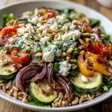 Overhead view of a Mediterranean Farro Pasta Bowl tossed with a zesty olive oil dressing, showing wilted spinach and toasted pine nuts next to a lemon wedge.