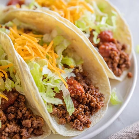 Close-up of fully loaded beef tacos showing melted cheese, salsa, and crunchy tortilla.