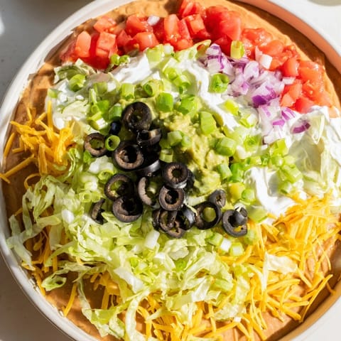 Vibrant layered Seven-Layer Dip, featuring refried beans, guacamole, and toppings, perfect for sharing and dipping.