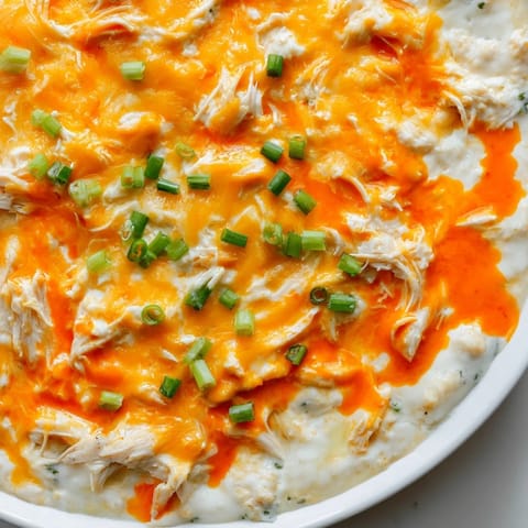 Close-up of creamy, spicy Buffalo Chicken Dip bubbling in a baking dish, ready to eat alongside snacks.