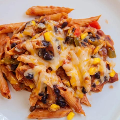 A fork lifts a serving of Chicken Enchilada Pasta, revealing juicy shredded chicken, black beans, and diced bell peppers nestled in cheesy pasta.