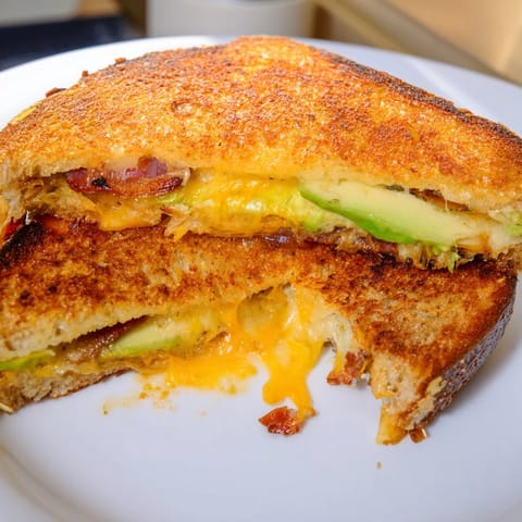 Gooey Avocado BLT Grilled Cheese halves stacked on a plate, showcasing ripe avocado, fresh lettuce, and crunchy bacon.