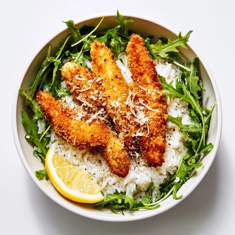 Golden, crispy Parmesan chicken cutlets sliced over fluffy white rice with fresh arugula and lemon wedges.