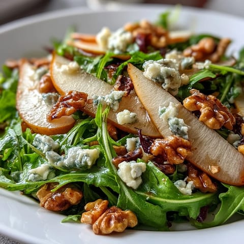 Fresh arugula and sliced ripe pears topped with crumbled blue cheese and crunchy toasted walnuts in a bowl.