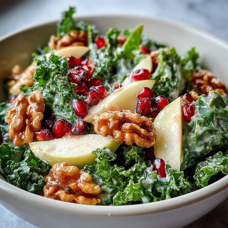 A close-up view of a vibrant kale and pomegranate bowl garnished with chopped walnuts and thin apple ribbons for a healthy lunch.