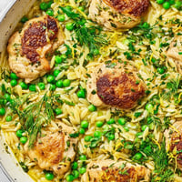 Golden-brown chicken pieces nestled in a creamy orzo skillet, garnished with fresh dill, parsley, and vibrant green peas in a zesty lemon sauce.