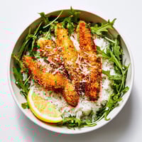 Golden, crispy Parmesan chicken cutlets sliced over fluffy white rice with fresh arugula and lemon wedges.