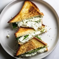 Slices of Whipped Feta Spring Grilled Cheese sit on a plate, with creamy filling peeking from golden, buttery bread.  