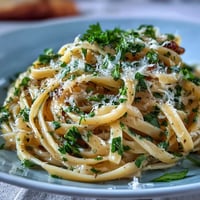 Creamy lemon butter pasta with peas and Parmesan, garnished with fresh parsley, in a white bowl with a side of lemon wedges.